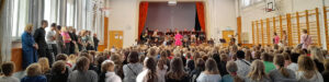 Orkesteri soittamassa koulun salissa, jossa istuu lapsia.